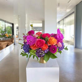 Bright mixed bouquet in a gold vase with pink, orange, purple, and blue blooms