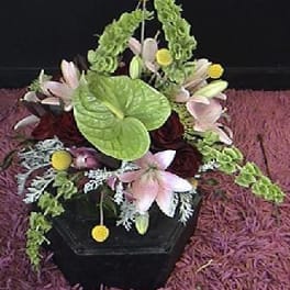 Floral arrangement in a black container with pink lilies and green accents
