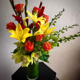 Bouquet of yellow lilies and orange roses in a green glass vase
