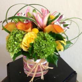 Bouquet of yellow roses, green hydrangeas, and pink lilies in a glass vase