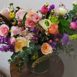 Large mixed bouquet of pink, peach, purple, and yellow flowers in a dark vase