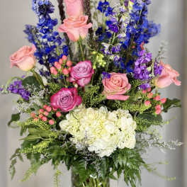 Tall bouquet of pink roses, blue flowers, and white hydrangeas in a glass vase