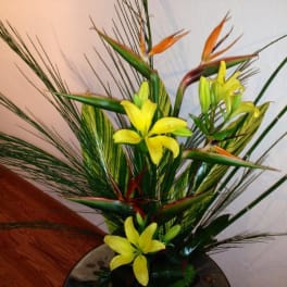 Tropical arrangement with yellow lilies and bird-of-paradise in a vase
