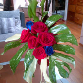Arrangement of red and blue roses with large variegated leaves in a vase