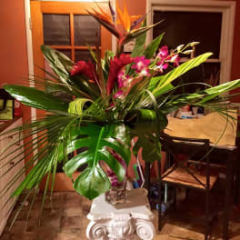 Tall tropical arrangement with pink orchids and orange bird-of-paradise in a glass vase