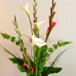 Tall floral arrangement with white calla lilies and red gladiolus in a glass vase