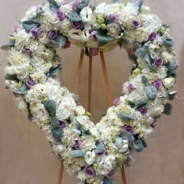 Heart-shaped floral wreath of white blooms and lavender roses on a stand