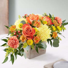Low arrangement of orange roses and yellow mums in a rustic wooden box.