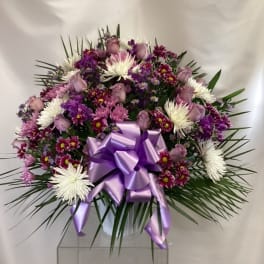 Lavender and white floral arrangement with a purple ribbon in a white container