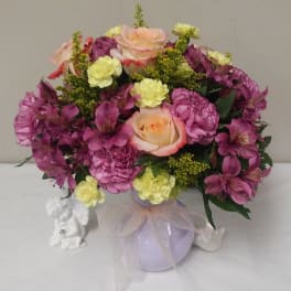 Mixed bouquet of pink and yellow flowers in a lavender vase with a ribbon
