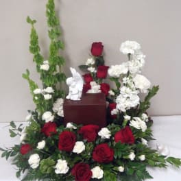 Red roses and white flowers arranged around a small urn with a figurine