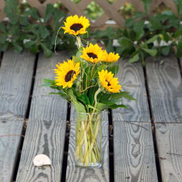 Sunflowers arranged in a clear glass vase on a wooden deck
