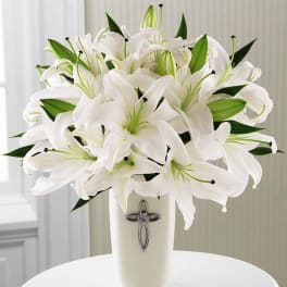 White lilies arranged in a tall vase with a cross emblem