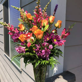 Tall bouquet of orange roses, pink snapdragons, and purple daisies in a glass vase
