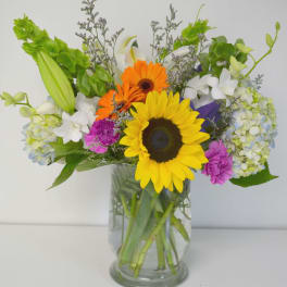 Mixed bouquet with sunflowers, gerbera daisies, lilies, and hydrangeas in a glass vase