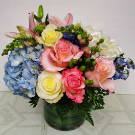 Mixed bouquet of roses, hydrangeas, lilies, and orchids in a green vase