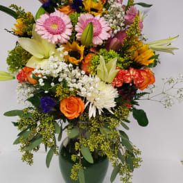 Mixed bouquet of pink gerbera daisies, sunflowers, roses, and lilies in a vase