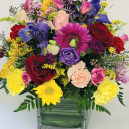 Mixed bouquet in a square glass vase with roses, daisies, and colorful blooms