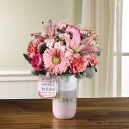 Pink bouquet in a white and pink vase with a baby tag
