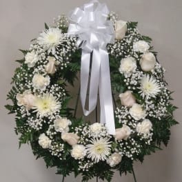 White funeral wreath with roses, daisies, and a large ribbon bow
