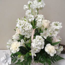 White floral arrangement in a woven basket with a pink ribbon handle