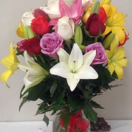 Mixed bouquet of lilies and roses in a glass vase with a red ribbon