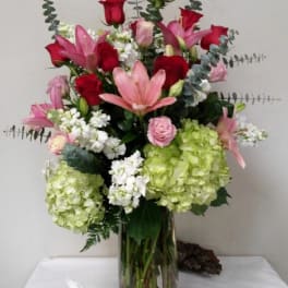 Tall bouquet of red roses, pink lilies, and green hydrangeas in a glass vase