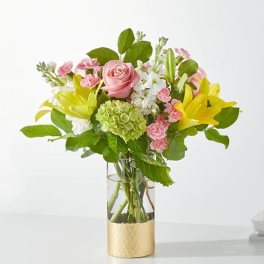 Pink roses and yellow lilies in a glass vase with a gold base