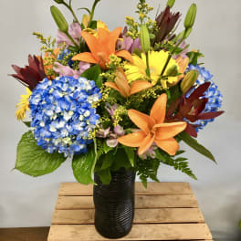 Colorful bouquet with lilies, hydrangeas, and gerbera daisies in a black vase