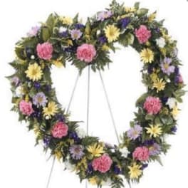 Heart-shaped floral wreath on a stand with pink, yellow, purple, and white flowers