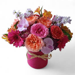 Mixed bouquet of pink, peach, and lavender flowers in a pink wrapped vase
