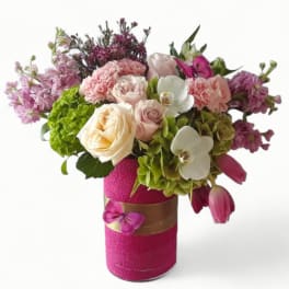 Vase of mixed pink, peach, and white flowers with orchids and tulips in a bright pink wrapped container