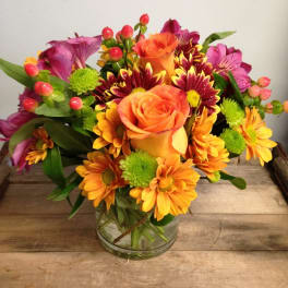 Mixed bouquet of orange roses, daisies, and purple flowers in a glass vase
