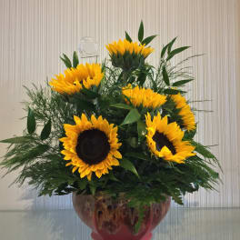 Sunflower arrangement in a glass bowl vase with dense greenery