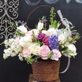 Basket arrangement of pink, white, and purple flowers with a ribbon bow