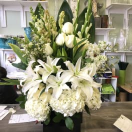 Large white floral arrangement with lilies and hydrangeas in a black container