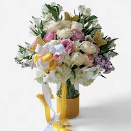 Pastel bouquet of roses, hydrangeas, and orchids in a vase with yellow ribbons and butterflies