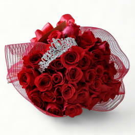 Round bouquet of red roses wrapped in red mesh with a silver tiara nestled on top.