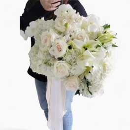 Large hand-tied bouquet of white roses, lilies, hydrangeas, and orchids with long white ribbon tails