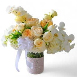 Cream roses and white orchids arranged in a glass vase with a ribbon