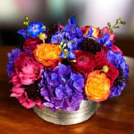 Bright mixed bouquet in a low silver vase with purple, pink, and orange blooms