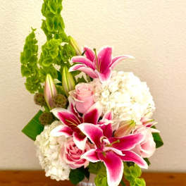 Pink lilies and roses arranged with white hydrangeas in a white vase