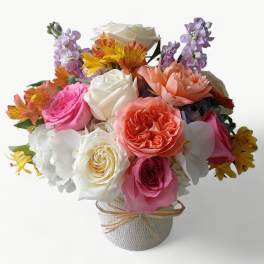 Mixed bouquet of roses, orchids, and alstroemeria in a white textured vase with raffia tie