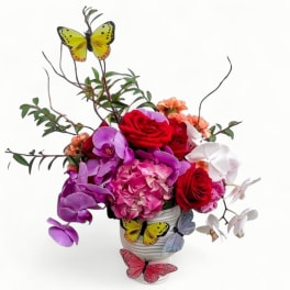 Colorful arrangement of roses, orchids, hydrangea and carnations in a white vase with decorative butterflies
