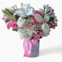 Tall vase arrangement of white lilies and roses with pink mixed blooms and ribbon.