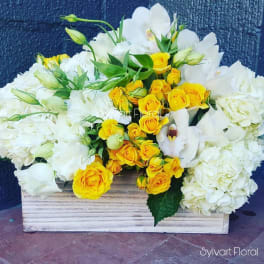 White hydrangeas and yellow roses arranged in a wooden box