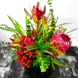 Bright tropical flower arrangement in a black vase with red berries
