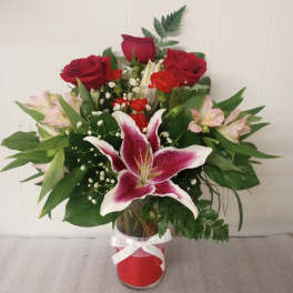 Red roses and pink lilies in a glass vase with a white ribbon