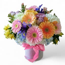 Colorful bouquet of gerbera daisies, roses, and irises in a wrapped vase