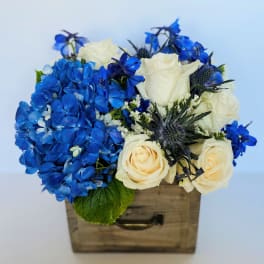 Blue hydrangeas and white roses arranged in a wooden box